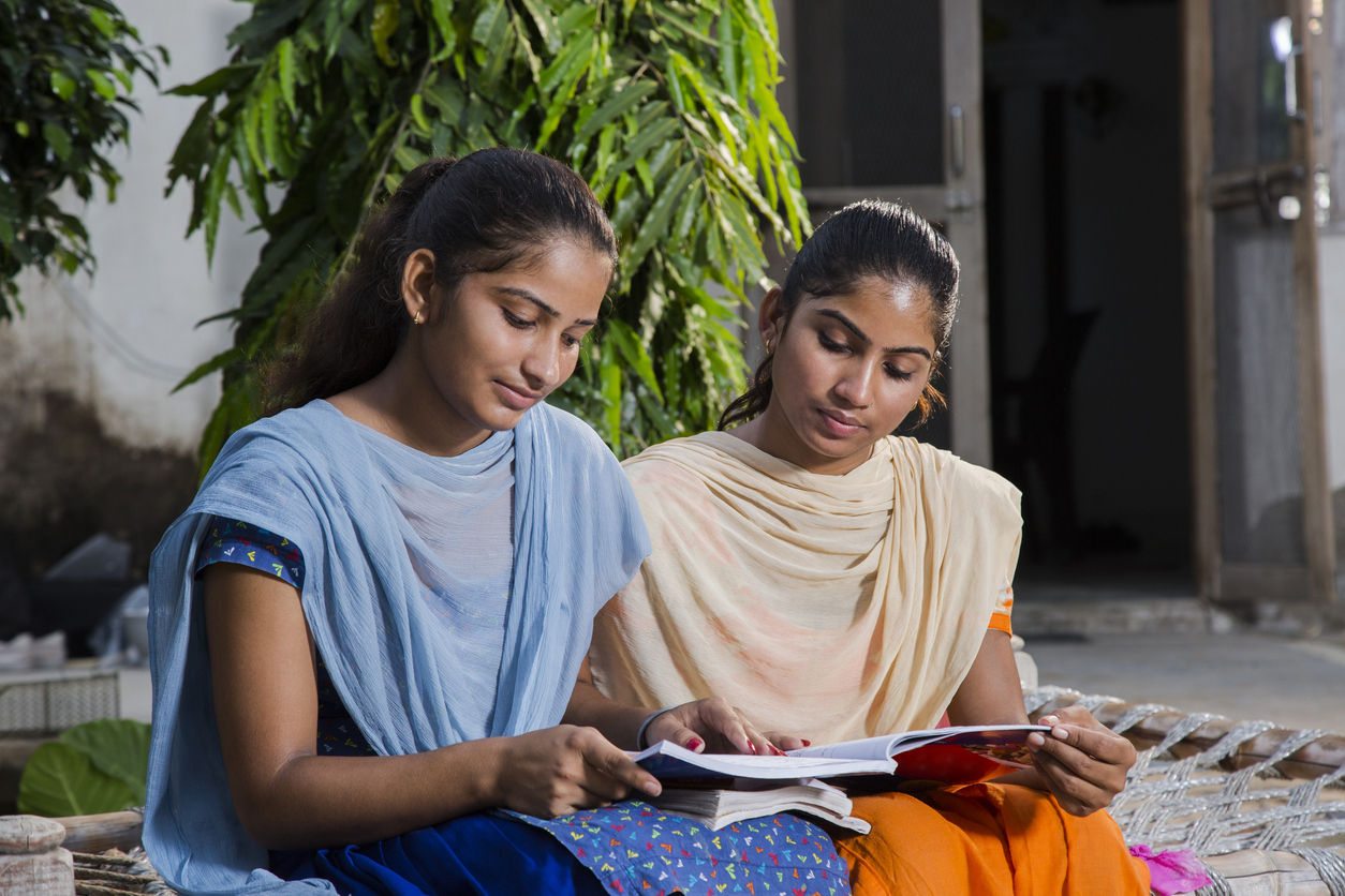 Two women in classical India dress, seated on a step, studying