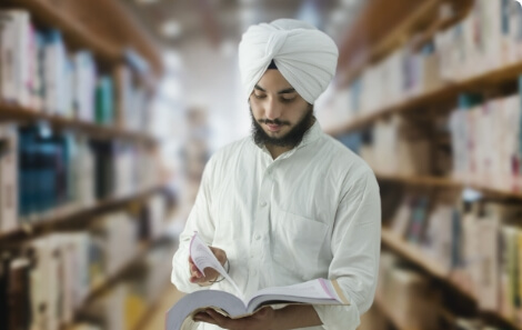 Man in a turban and white shirt, reading a notebook